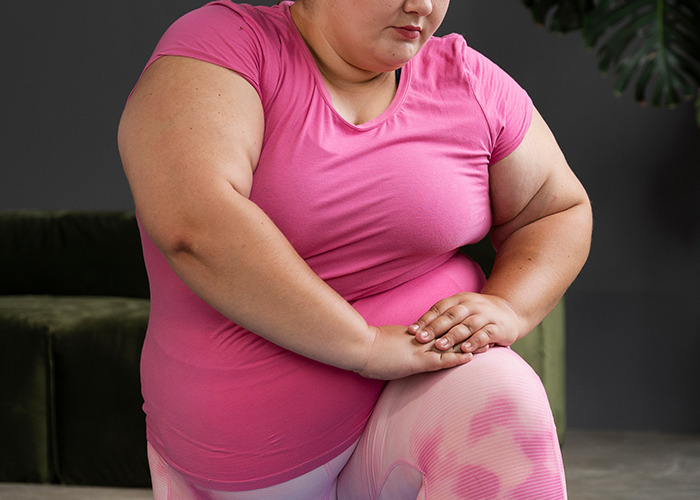 Woman in pink shirt sitting with hands on knee, reflecting on personal experiences of being gaslit by a doctor.