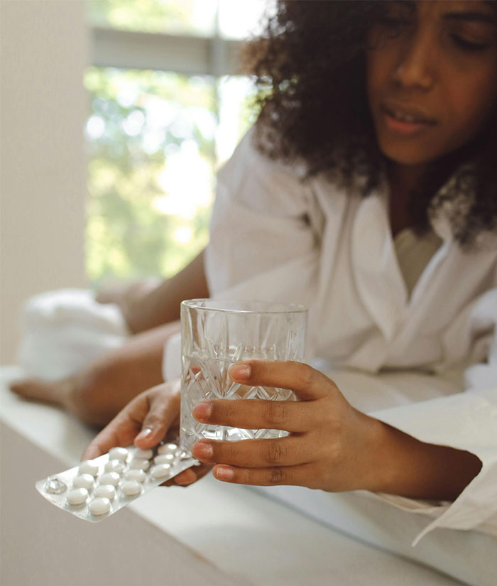 Person in a white robe holding a glass of water and a pill blister pack, highlighting European pharmacies medication packaging. Person in a white robe holding a glass of water and a pill blister pack, highlighting European pharmacies medication packaging.