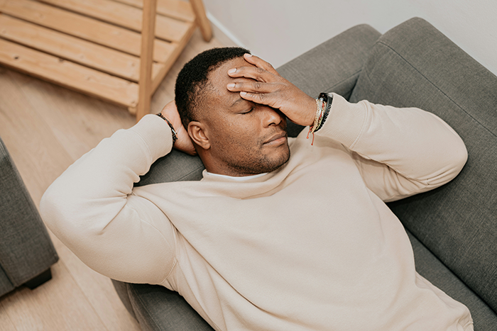 Man crushed after wife cheats, resting on couch with hand on forehead, reflecting pain and emotional struggle. - 28