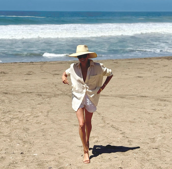 Meghan Markle walking on the beach in a wide-brimmed hat and light outfit amid fruit-picking photo fraud accusations.
