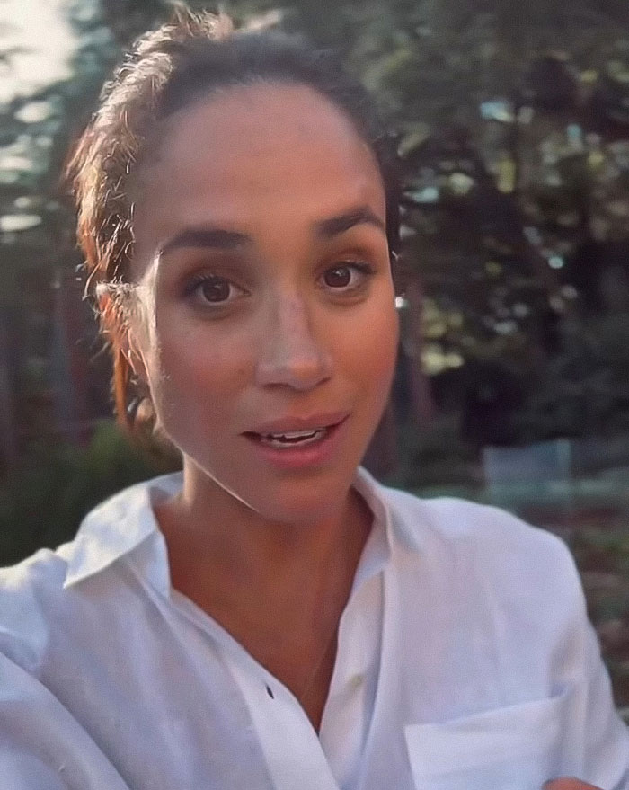Meghan Markle in a white shirt outdoors with trees in the background, linked to fruit-picking photo accusations.