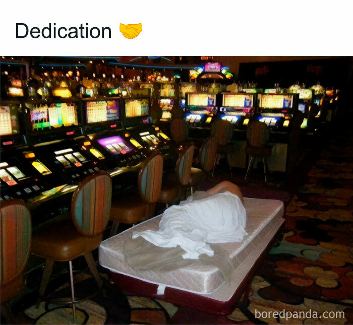 Person sleeping wrapped in a blanket on a mattress in a casino near slot machines, illustrating dedication in chaotic memes.