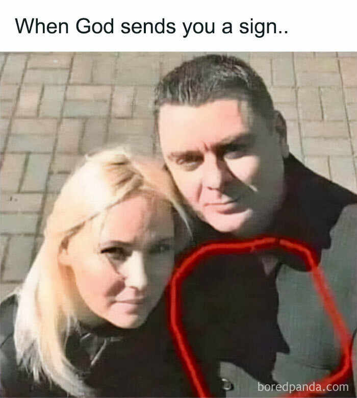 A man and woman taking a selfie with a shadow that forms a funny, chaotic random face outline on the wall behind them.