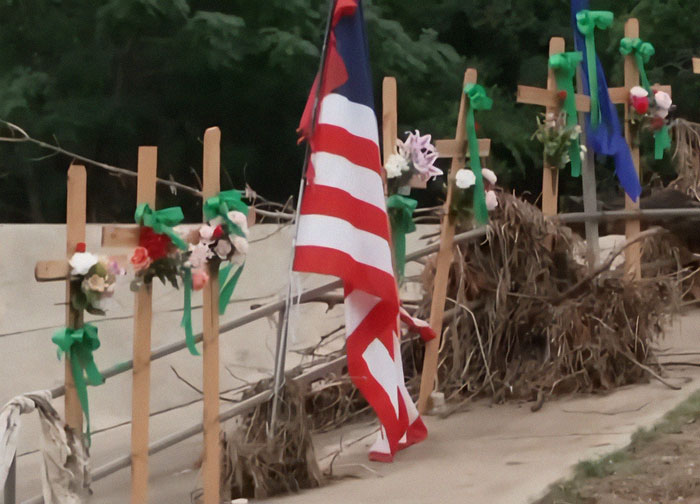 Memorial crosses with flowers and an American flag honoring the Camp Mystic tragedy victims in an outdoor setting. - 1