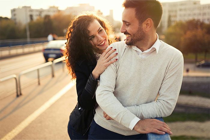 A happy couple outdoors, with the woman smiling and leaning on the man, highlighting challenges men explain to women.