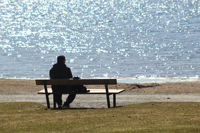 Man sitting alone on a bench by the water, reflecting on the hardest things to explain to women that drives his wife crazy.