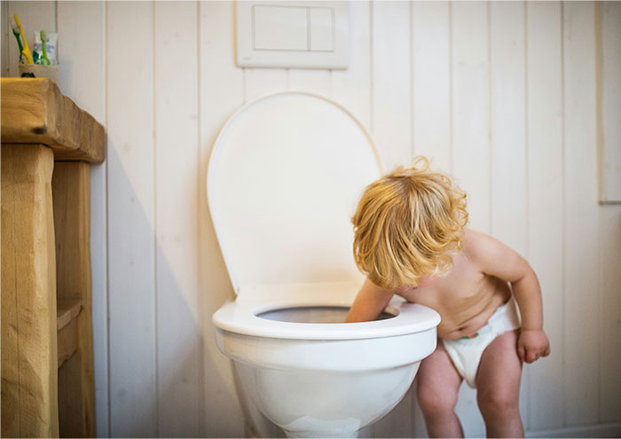 Young toddler in diaper exploring and looking into a toilet bowl, a challenge that drives many wives crazy to explain.