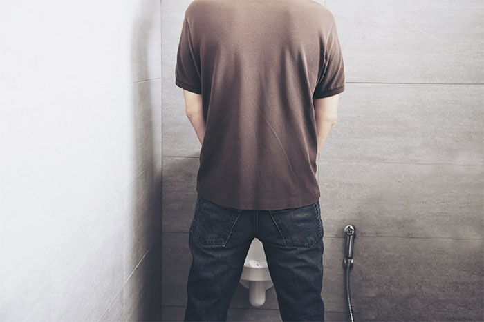 Man standing at a urinal in a restroom, illustrating the hardest things men try to explain to women.