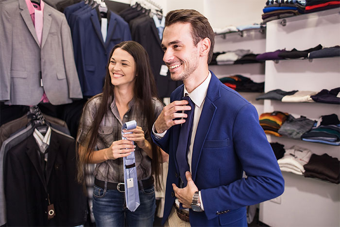 Man trying on a suit while woman holds a tie, illustrating challenges men face explaining things that drive their wives crazy.