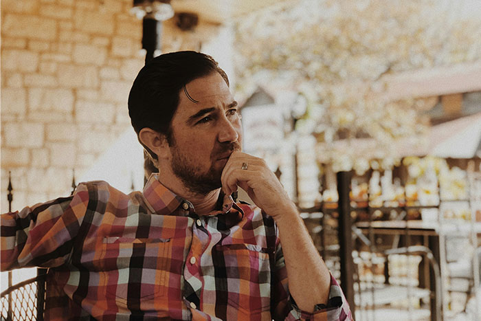 Man in a plaid shirt sitting outdoors, deep in thought, representing the hardest things men try to explain to women.