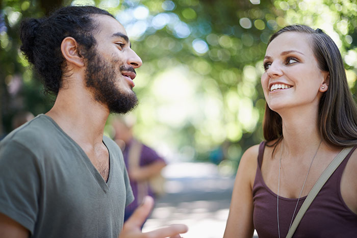 A man and woman smiling and talking outdoors, illustrating things men shouldn't do while pursuing women. - 15