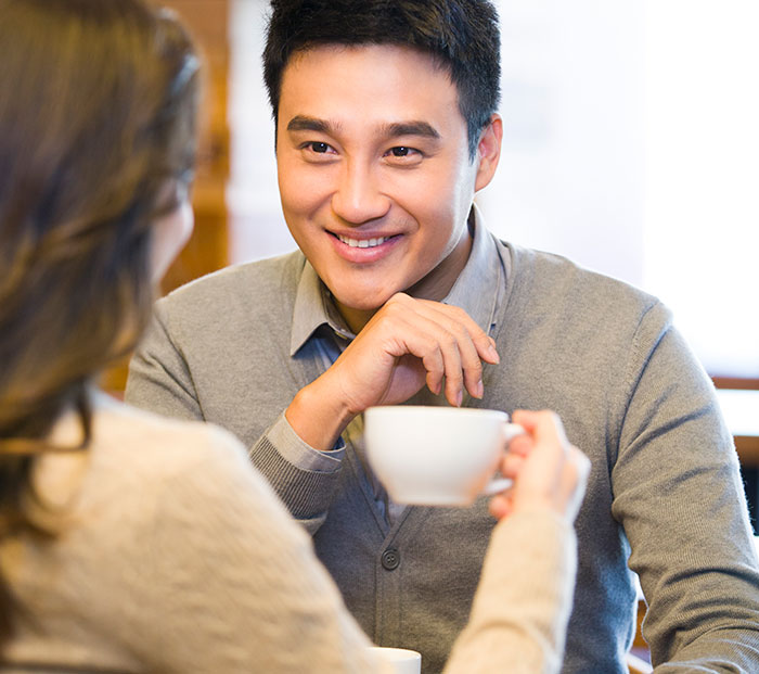 Man smiling and having coffee with woman, illustrating things men shouldn’t do while pursuing women advice online. - 12