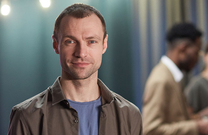 Man in casual clothes smiling slightly in a social setting, relating to things men shouldn’t do while pursuing women online. - 31