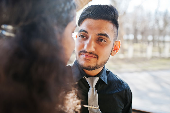 Young man wearing a silver tie attentively listening to a woman during a conversation about things men shouldn’t do while pursuing women. - 28