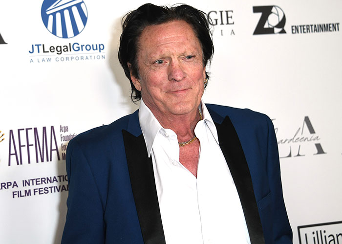 Actor Michael Madsen attends a film festival event, dressed in a blue suit jacket and white shirt, smiling for cameras.