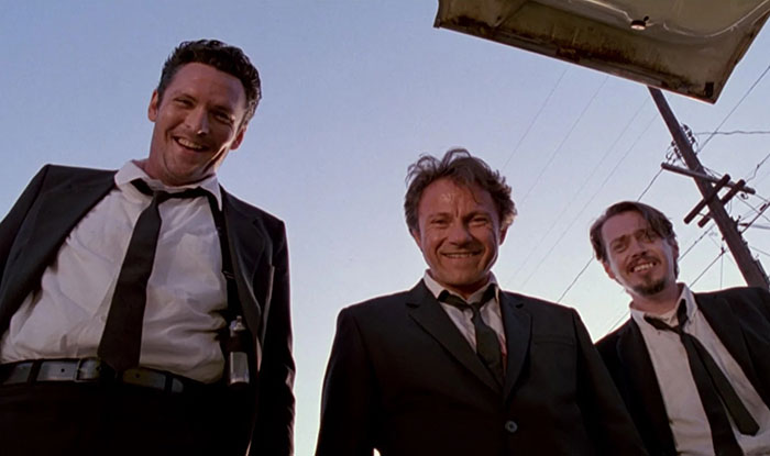 Three men in black suits and ties smiling while standing outdoors under a clear sky, related to actor Michael Madsen tribute.