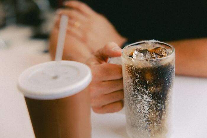 Close-up of hand holding iced cola glass with condensation and ice, illustrating surprising things travelers share about the U.S.