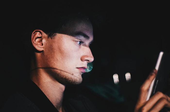 Young man focused on his smartphone screen at night, illustrating micro cheating stories and trust issues.