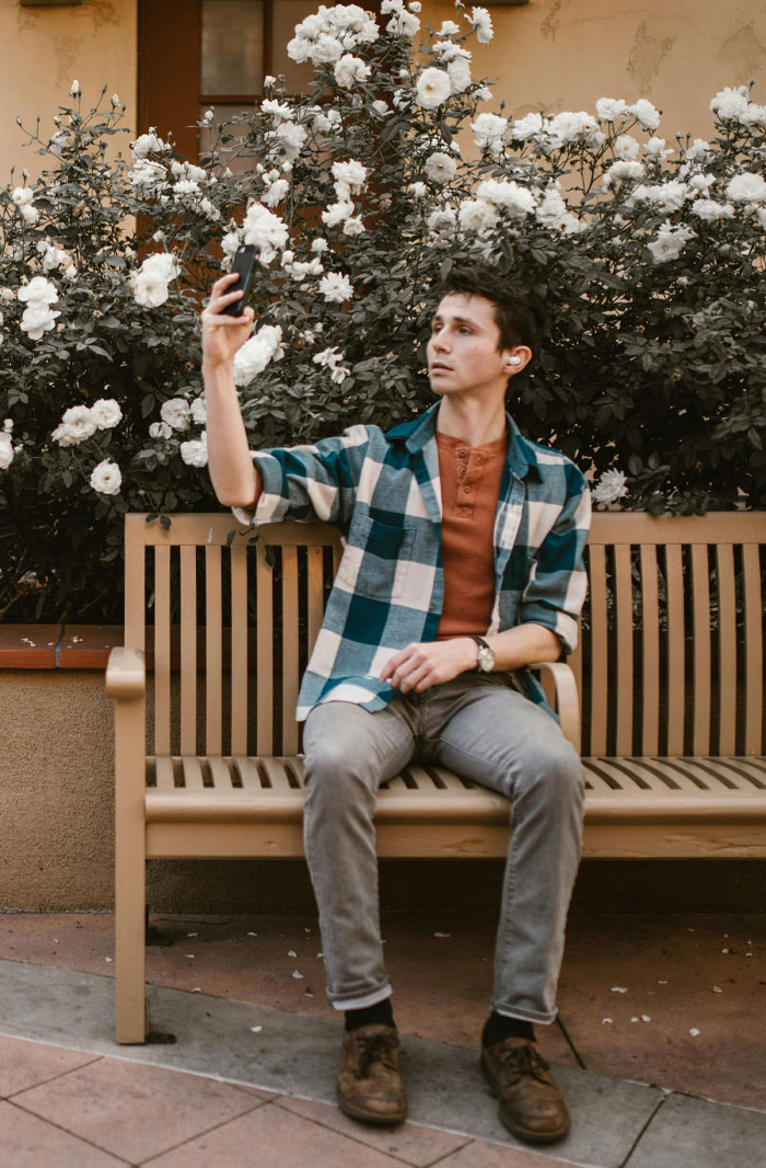 Young man sitting on a bench using phone earbuds, illustrating micro cheating stories and trust issues in relationships outdoors.