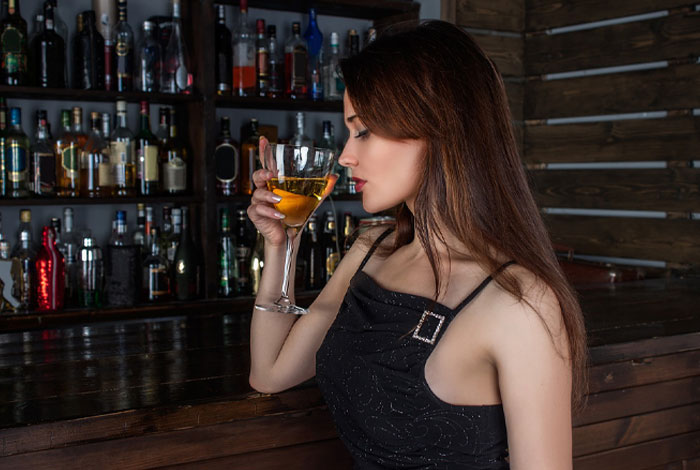 Young woman in a black dress holding a cocktail glass in a bar setting, illustrating micro cheating stories concept.
