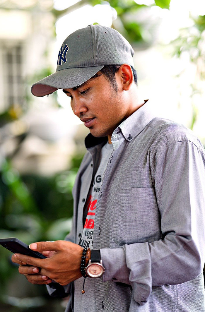 Young man wearing a cap and casual shirt checking his phone, representing micro cheating stories and trust issues.
