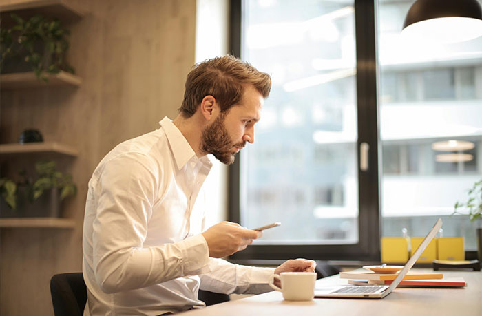 Man in white shirt checking phone with concerned expression, illustrating micro cheating stories in a modern office setting.