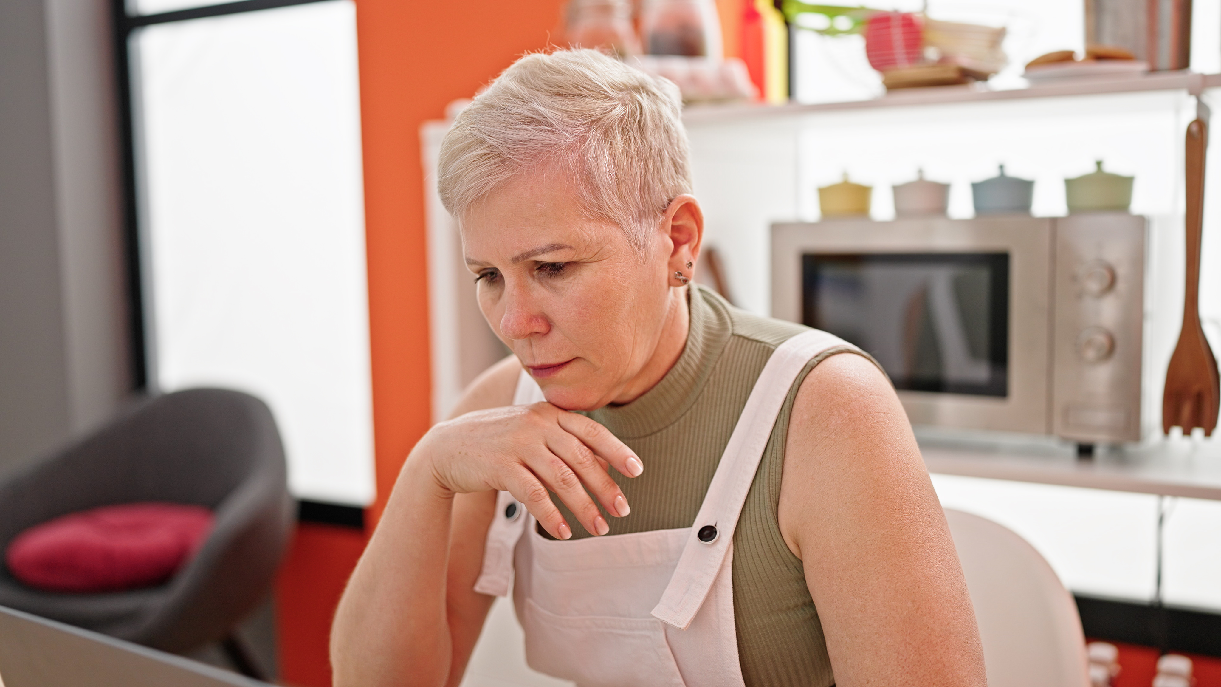 Older woman looking concerned while using a laptop at home, representing family drama over inherited house and rent-free living.