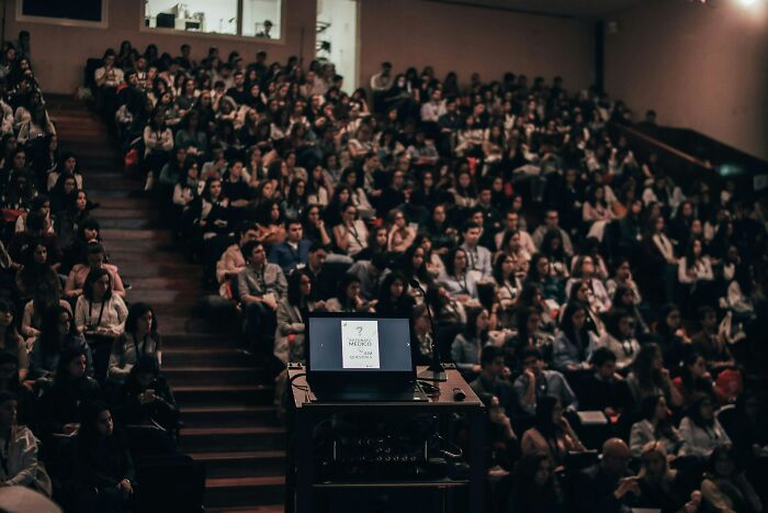 Audience in a dark auditorium watching a presentation, illustrating people who deal with dead bodies uncovering weird details.