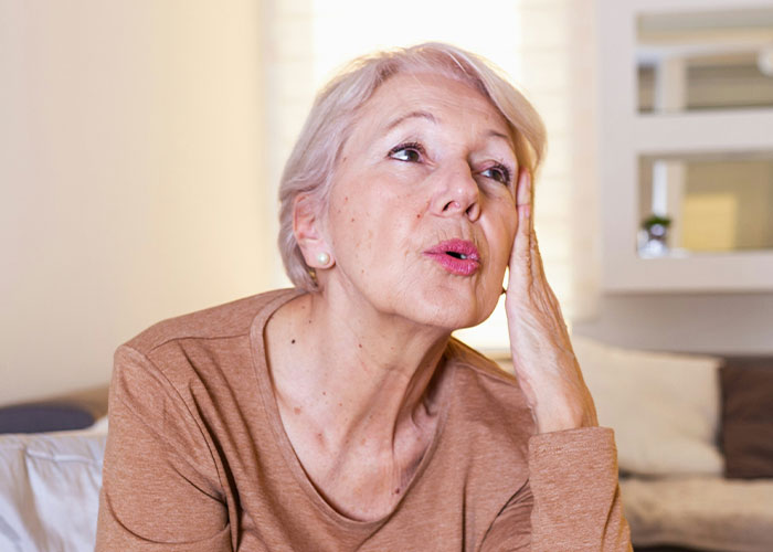 Elderly woman battling cancer looking concerned while sitting indoors, depicting struggle and emotional distress. - 9