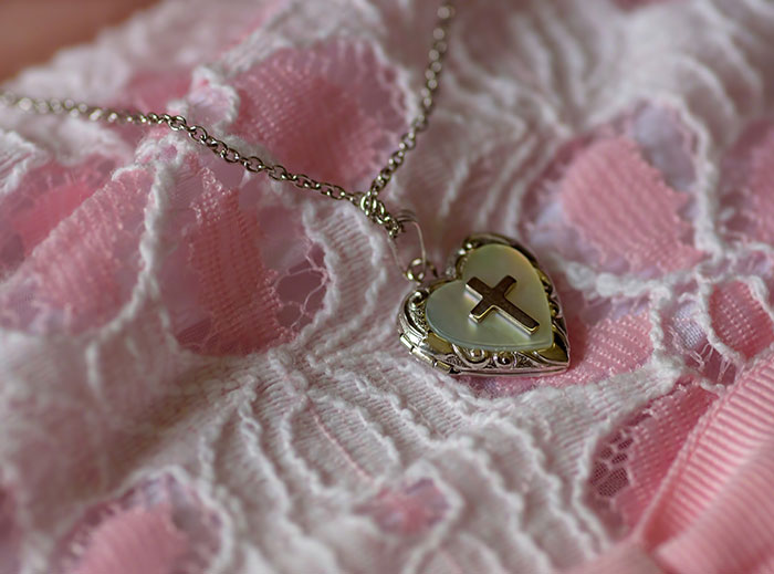 Heart-shaped locket with a cross resting on pink lace fabric, symbolizing family drama and grandson's ashes conflict.