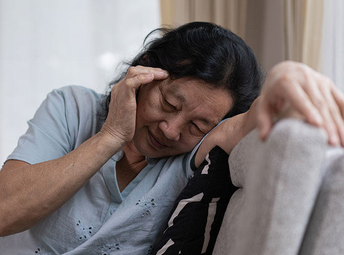 Elderly woman looking distressed on a couch, reflecting family drama involving grandson&rsquo;s ashes and entitled grandma actions.