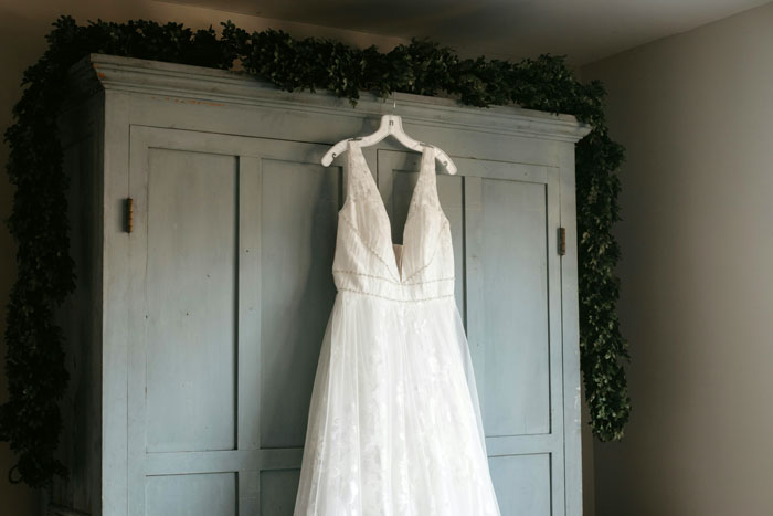 White wedding dress hanging on a hanger in a room decorated with greenery, symbolizing bride's wedding power struggle. White wedding dress hanging on a hanger in a room decorated with greenery, symbolizing bride's wedding power struggle.