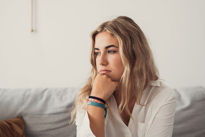 Young woman in white shirt sitting thoughtfully, reflecting on a bride’s wedding power struggle with mother-in-law. Young woman in white shirt sitting thoughtfully, reflecting on a bride’s wedding power struggle with mother-in-law.