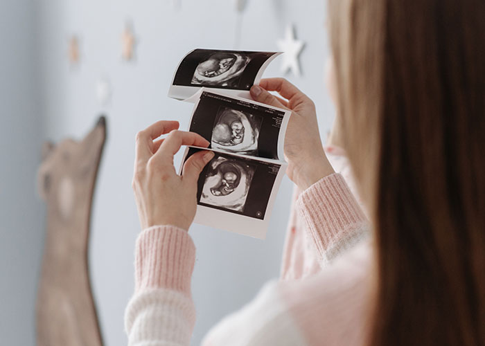 Woman in pink sweater holding and looking at ultrasound photos related to gender reveal and family dynamics.
