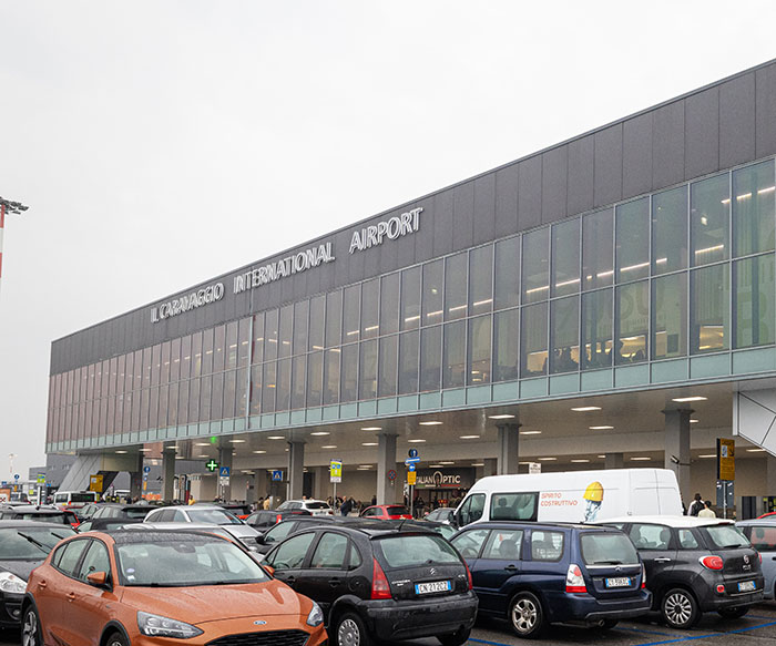 Il Caravaggio International Airport exterior with parked cars representing scene related to man sucked into plane engine incident.