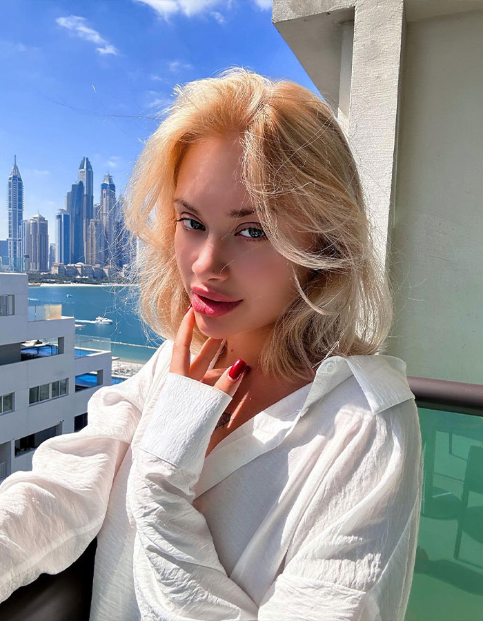 Young blonde woman posing on Dubai balcony with skyline in background representing model's mom and scalped story. - 2
