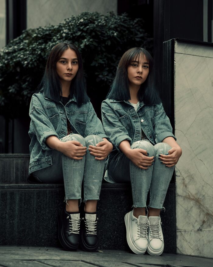 Two young women wearing matching denim jackets and jeans sitting side by side, illustrating awful roommates concept.