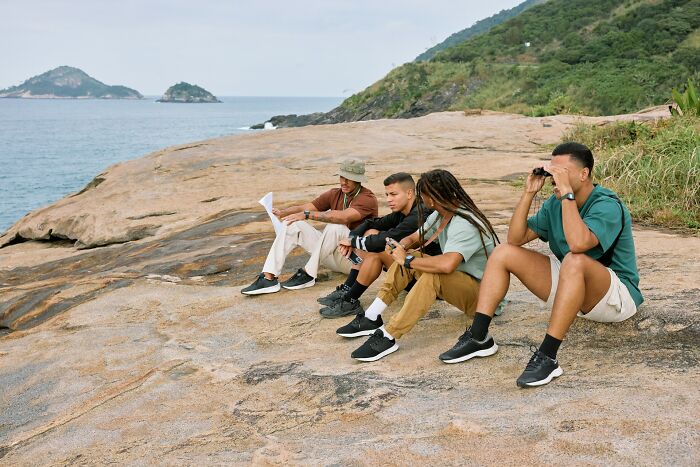 Four men sitting on a rocky shore, enjoying nature and sharing moments that seem bizarre to women.