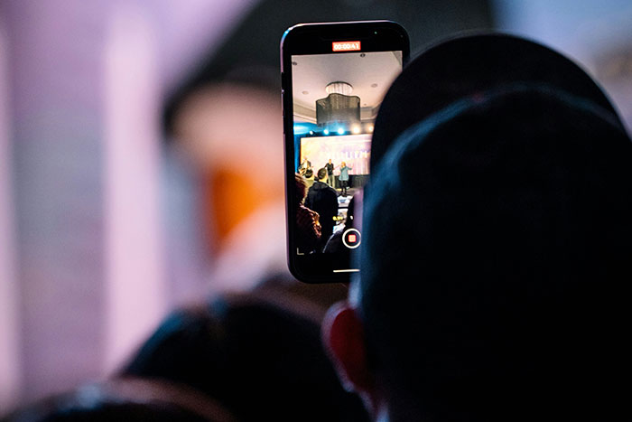 Person recording event on smartphone, illustrating man facing legal consequences as a deadbeat dad in public setting
