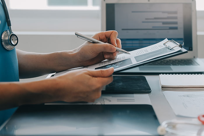 Man reviewing legal documents related to deadbeat dad consequences, holding pen and clipboard near laptop and medical tools.