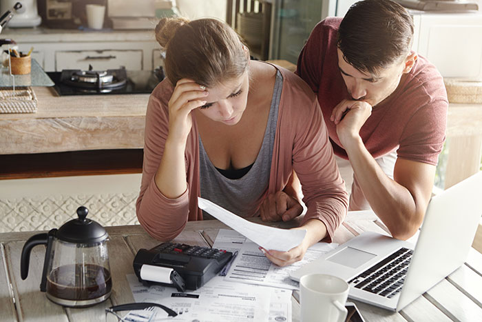 Mom faces money issues while husband advises budgeting, both reviewing bills and finances at a kitchen table. Mom faces money issues while husband advises budgeting, both reviewing bills and finances at a kitchen table.