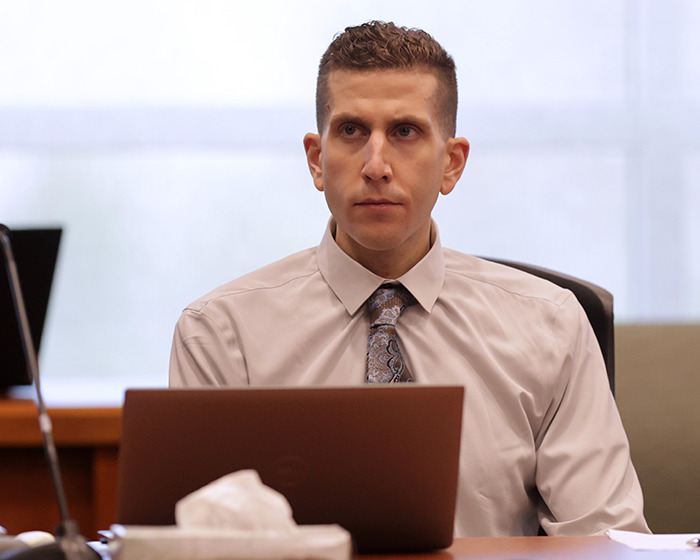 Man in a dress shirt and patterned tie sitting at a desk with a laptop, related to Bryan Kohberger's victim massacre case.
