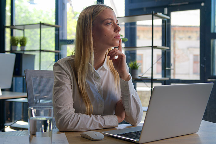Young woman sitting at desk with laptop, looking thoughtful and concerned while reflecting on friendships and trust issues.