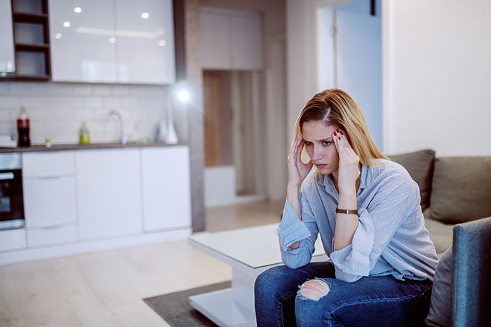 Young woman sitting in living room looking stressed, reflecting on friends who turned out to be total jerks.