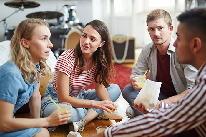 Four young adults having a serious conversation while sitting on the floor, reflecting on friends who are total jerks.