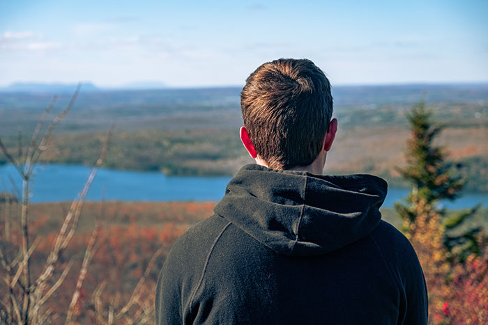Person wearing a black hoodie looking at a scenic autumn landscape, reflecting on friends who were actually jerks.