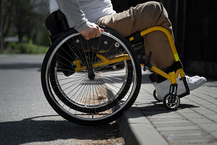 Person in a yellow wheelchair attempting to navigate a curb outdoors, highlighting challenges faced by people with mobility issues.