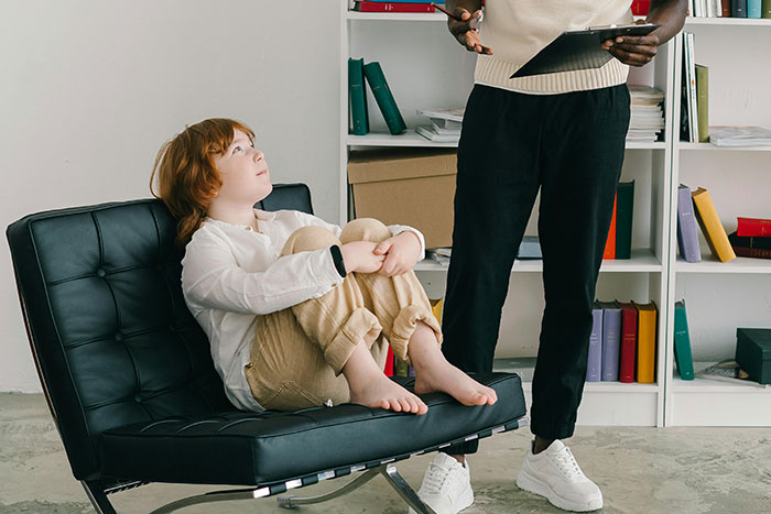 Child sitting barefoot on a chair looking up at standing adult during a real-life encounter with psychopaths session. - 5