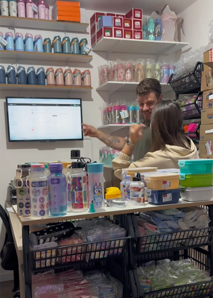 Momfluencer working in home office surrounded by colorful water bottles and storage containers on shelves and desk.