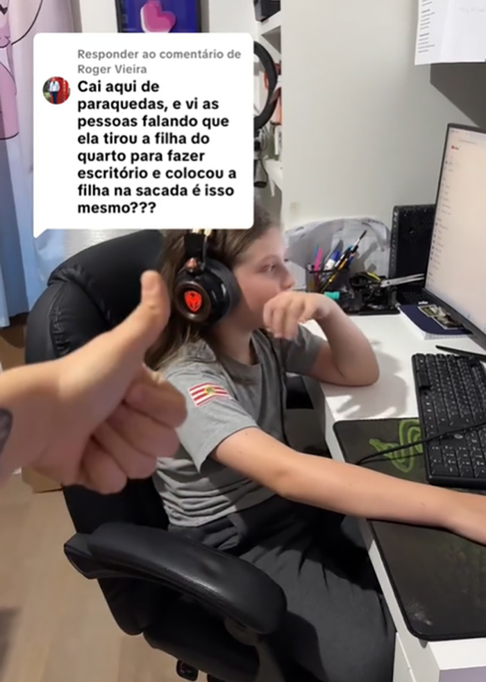 Child wearing headphones using a computer in an office setup while a hand shows thumbs up in the foreground.